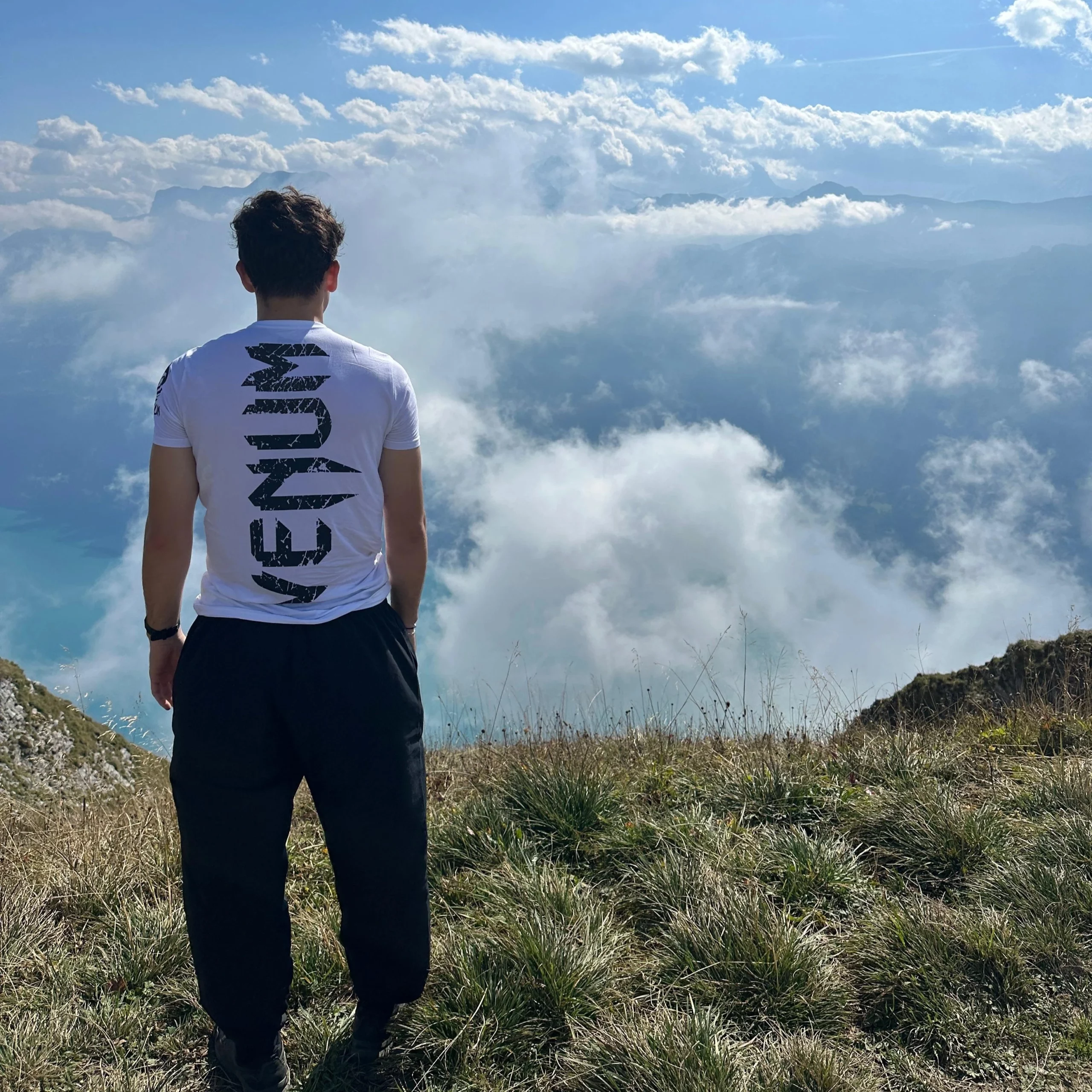 Homme se tenant sur une collline de dos regaardant au loin, ciel bleu, nuage blanc