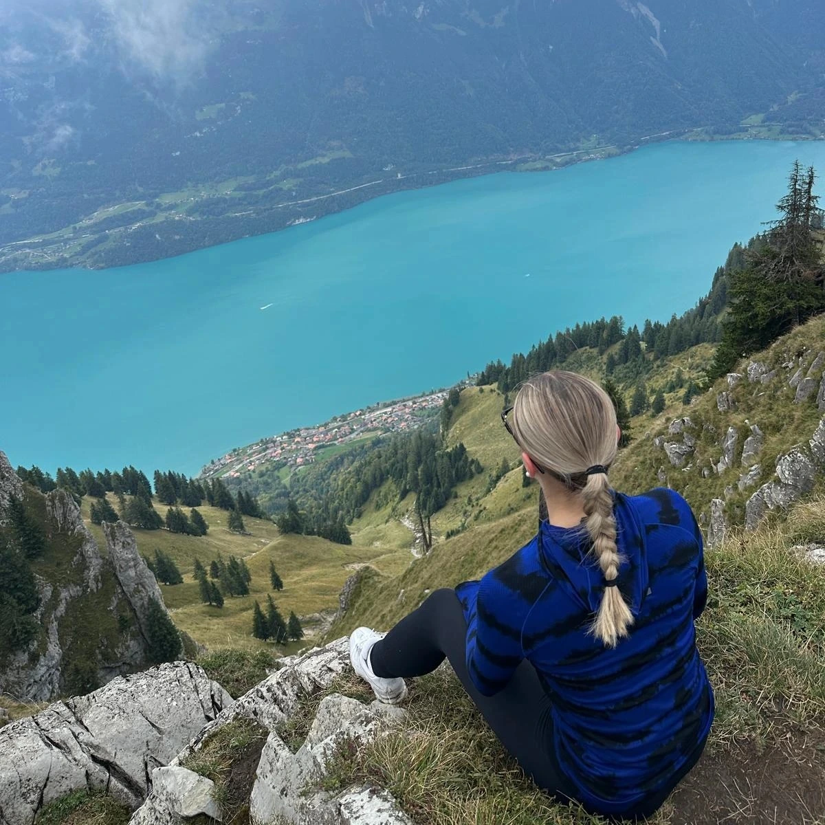 Femme de dos assise sur une pente, Lac bleu au loin, paysage Suisse