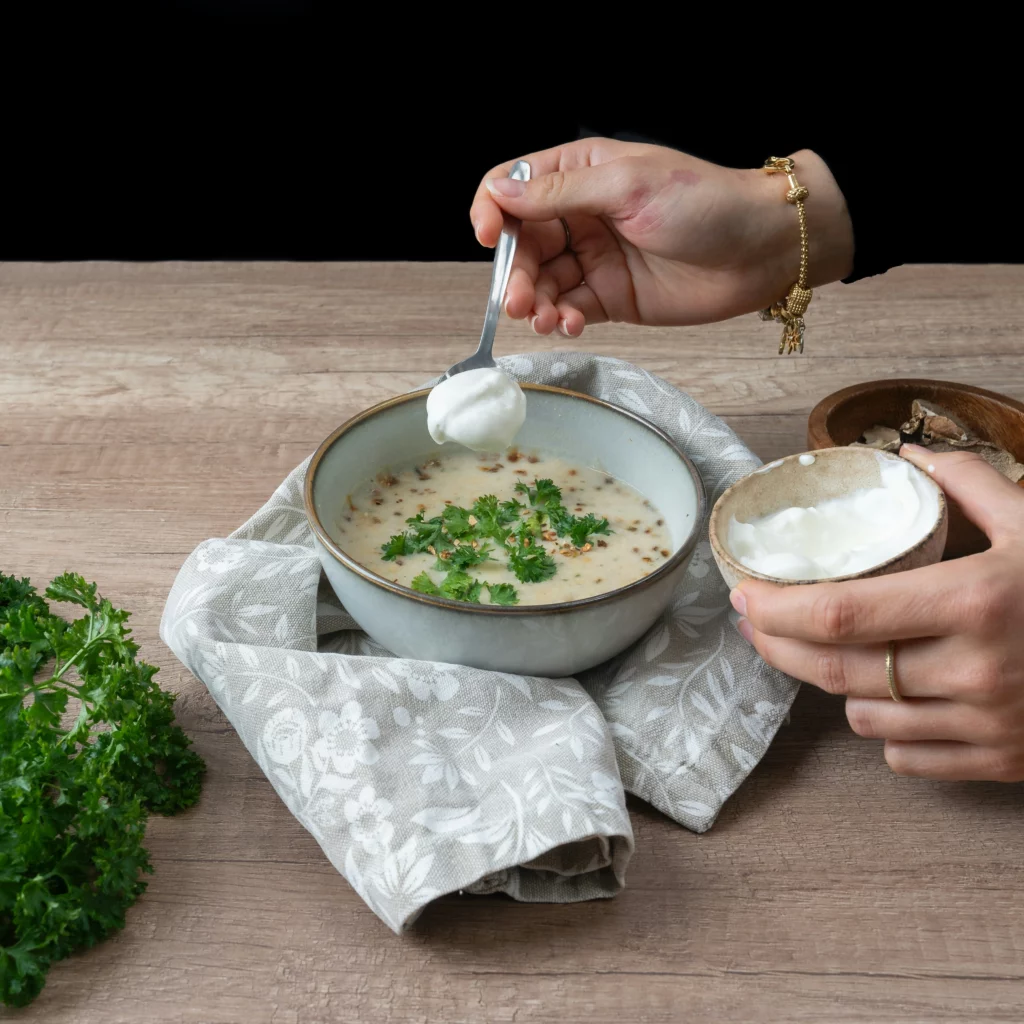 Soupe aux légumes, de couleur grisâtre une main de quelqu'un qui y rajoute de la crème