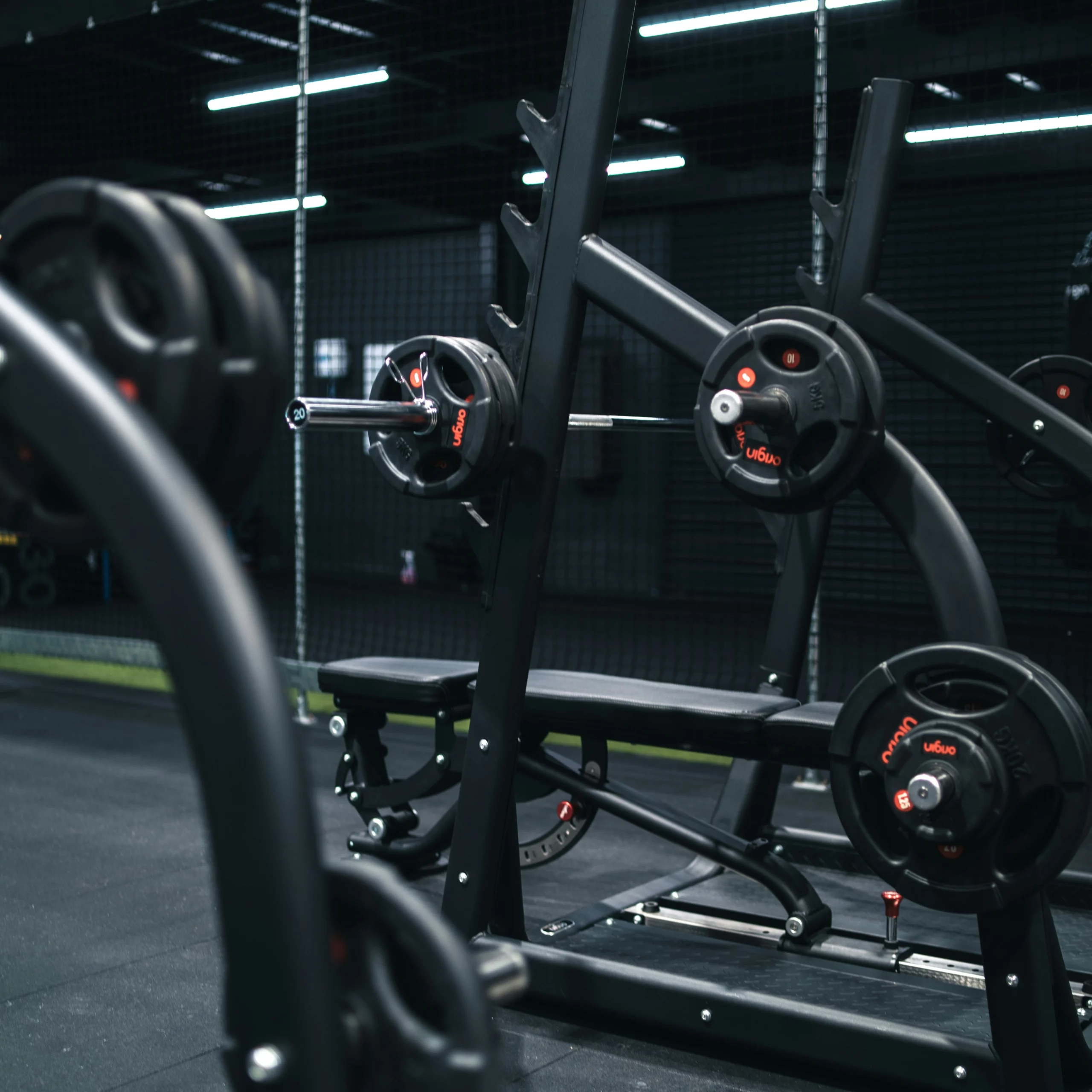 Salle de sport intérieure sombre, avec smith machine et poids.